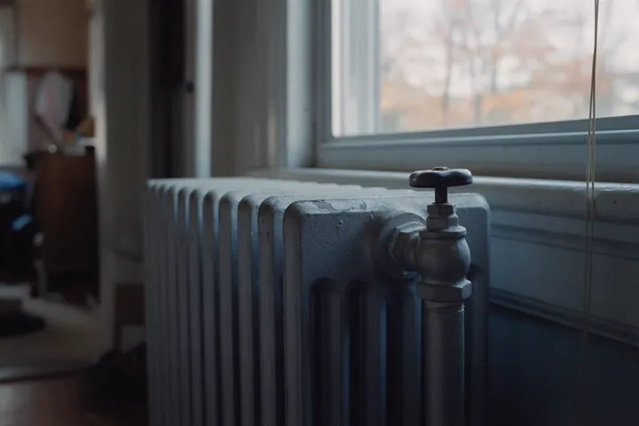 A cast iron radiator valve under a window, paint chipped back to bare metal.